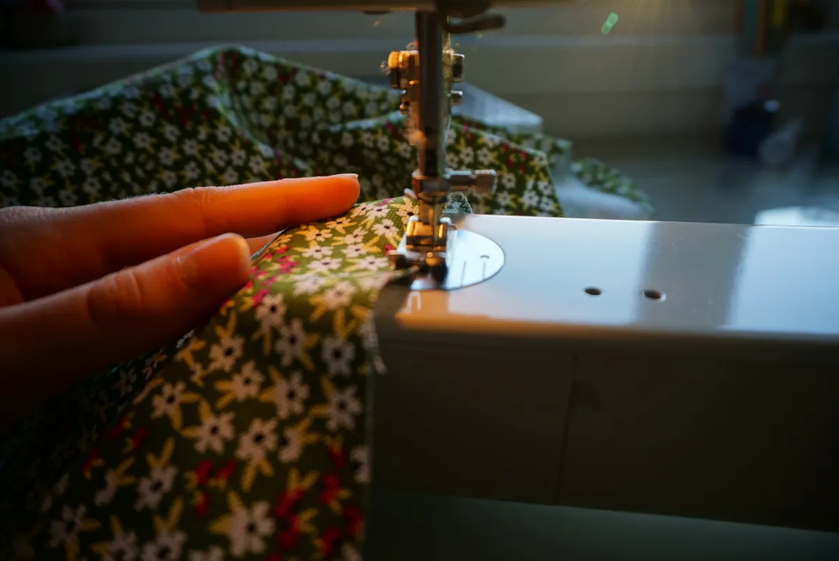Det gr&oslash;nne, hvite og r&oslash;de, blomstrete stoffet f&oslash;res gjennom en symaskin.
